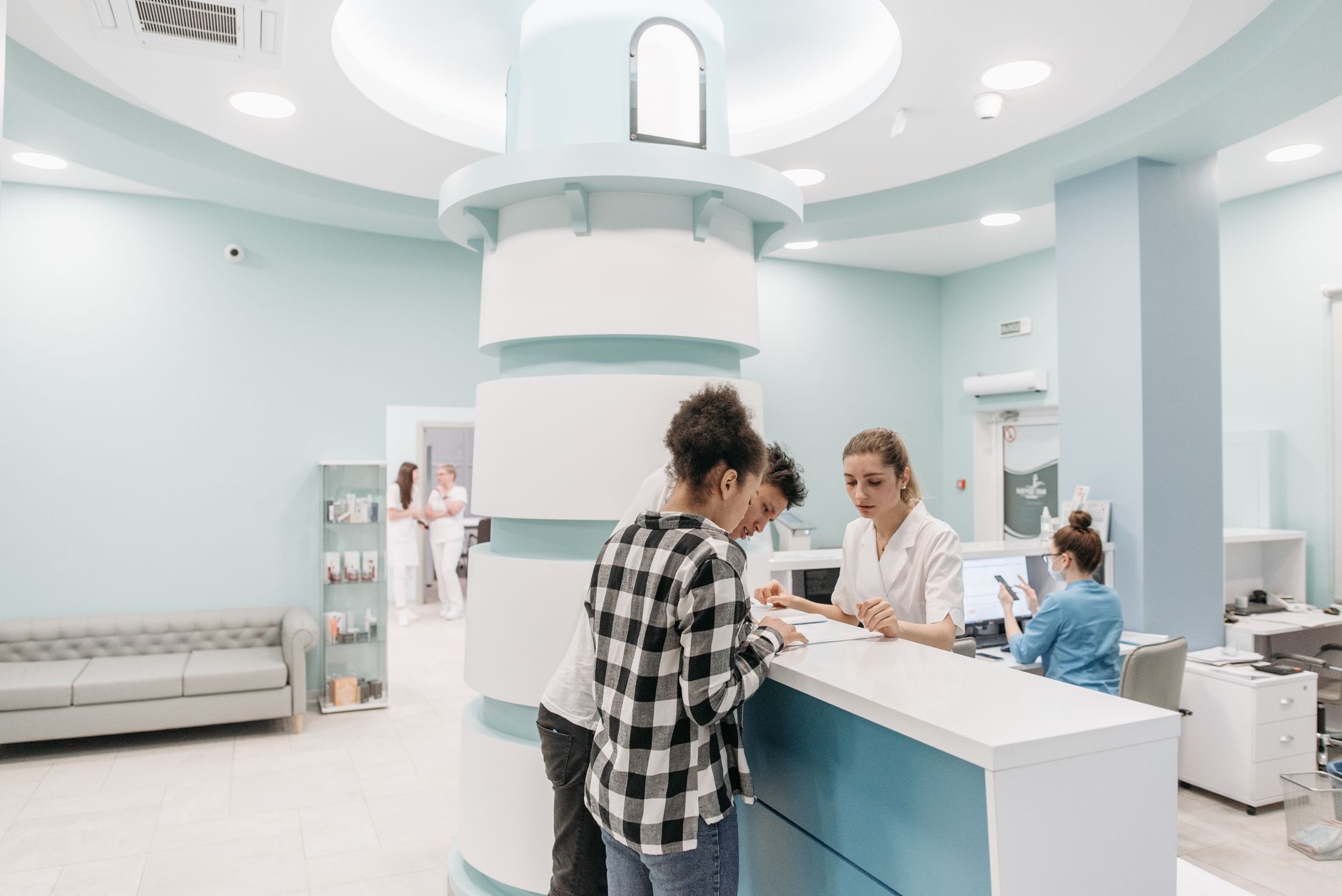 Patients complete registration at a clinic reception desk while staff help with forms and records